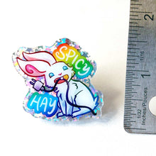 Load image into Gallery viewer, A glittery acrylic pin featuring a character from Rainbow of Crazy Comics: a smiling white rabbit holding a charging cable in her mouth, with the words "SPICY HAY in rainbow colours.
