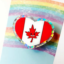 Load image into Gallery viewer, A glittery heart shaped acrylic pin featuring a character from Rainbow of Crazy Comics: the Canada flag with a stylized maple leaf with a happy face.
