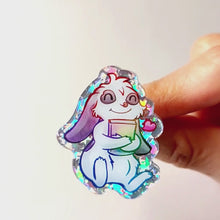 Load and play video in Gallery viewer, An acrylic pin featuring a character from Rainbow of Crazy Comics: a mini lop rabbit hugging a book, with a tiny heart next to him.
