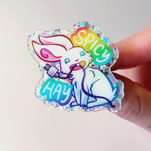 Load and play video in Gallery viewer, A glittery acrylic pin featuring a character from Rainbow of Crazy Comics: a smiling white rabbit holding a charging cable in her mouth, with the words "SPICY HAY in rainbow colours.
