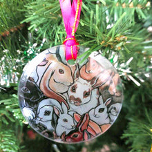 Load image into Gallery viewer, a round glass ornament, printed with a collage of different rabbit breeds, hanging from a Christmas tree with a red ribbon and gold string
