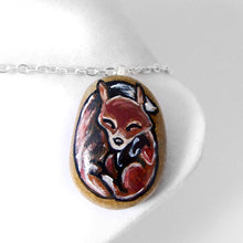 Load image into Gallery viewer, a small beach stone, hand painted with a portrait of a sleeping red fox, available as a keepsake, magnet, or necklace
