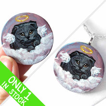 Load image into Gallery viewer, a small wood circle, hand painted with the portrait of a dark gray scottish fold cat, as an angel, with halo and wings, sitting on clouds against a pink and purple sky. available as a wood keepsake or pendant necklace
