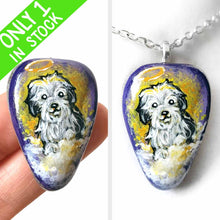 Load image into Gallery viewer, a beach stone hand painted with a sheepdog, as an angel with a halo, sitting on clouds against a purple and yellow sky. available as a keepsake or pendant necklace
