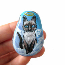 Load image into Gallery viewer, art of a siamese cat as an angel, is hand painted on a river rock, and is available as either a keepsake, fridge magnet,
 or a pendant necklace
