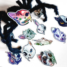 Load image into Gallery viewer, A set of colourful animal skull stickers, with a giant black furry spider decoration hovering above the stickers. One cat/skull sticker sits on top of the spider's face.
