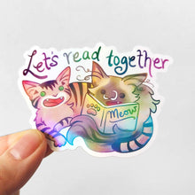 Load image into Gallery viewer, a sticker with two cats from Rainbow of Crazy Comics: a tabby cat next to a ragdoll cat that's holding a book titled "Meow". At the top of the sticker, it says, "Let's read together".
