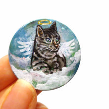 Load image into Gallery viewer, a small wood disc, hand painted with the portrait of a gray tabby cat, as an angel with wings and halo, sitting on clouds against a blue sky. this painting is available as a keepsake or pendant necklace
