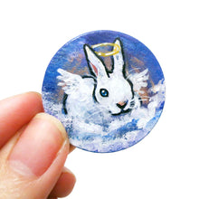 Load image into Gallery viewer, a wood disc, hand painted with the portrait of a white rabbit with blue eyes, painted as an angel, with halo and wings, sitting on clouds against a blue sky. available as a keepsake or pendant necklace
