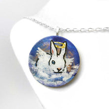Load image into Gallery viewer, a wood disc, hand painted with the portrait of a white rabbit with blue eyes, painted as an angel, with halo and wings, sitting on clouds against a blue sky. available as a keepsake or pendant necklace
