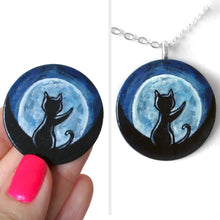 Load image into Gallery viewer, A lightweight wooden disc features art of the silhouette of a black cat, with a front paw reaching up, sitting in front of a big glowing full moon. Available as a keepsake, magnet or necklace
