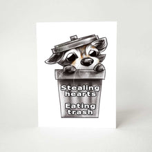 Load image into Gallery viewer, a birthday greeting card with art of a baby raccoon peeking out from a garbage can. the card reads, "stealing hearts. eating trash" on the front and
