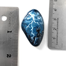 Load image into Gallery viewer, a beach rock with cat art: a black cat on a cliff, looking out into the night sky filled with lightning. the stone is next to two rulers to show its size: 1 9/16" x 1" or 4 cm x 2.5 cm
