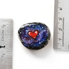 Load image into Gallery viewer, a beach stone has been hand painted with a heart surrounded by outer space and stars, and hand crafted as either a keepsake stone, magnet, or pendant necklace. it measures 1 3/16" x 1 1/16" or 3 cm x 2.7 cm
