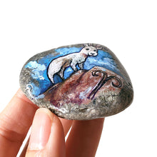 Load image into Gallery viewer, Rock art featuring a painting of a ram on a mountain, in front of a cloudy blue sky. The symbol for Aries is painted on the bottom.
