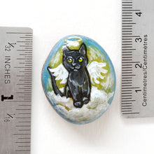 Load image into Gallery viewer, Rock art of a black cat as an angel, painted on a small beach stone, next to two rulers to show its size: 1 5/16" x 1 1/8" or 3.4 cm x 2.8 cm
