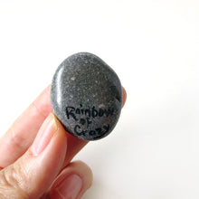 Load image into Gallery viewer, The back of a rock art of a black cat as an angel, signed with, "Rainbow of Crazy"
