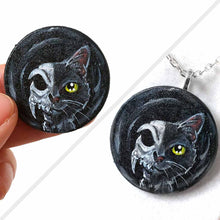 Load image into Gallery viewer, a circle shaped wood disc, hand painted with a split image: a black cat's face on the right side, and a cat skull on the left side. available as a keepsake or pendant necklace
