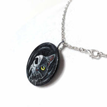 Load image into Gallery viewer, a circle shaped wood disc, hand painted with a split image: a black cat's face on the right side, and a cat skull on the left side. available as a keepsake or pendant necklace
