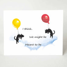 Load image into Gallery viewer, A greeting card printed with two black cats, each attached to a big balloon, floating in the sky towards each other. The text reads, "We might be Meant to be"
