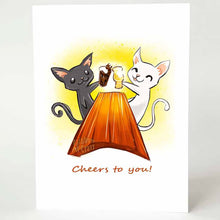 Load image into Gallery viewer, a greeting card, with art of a black cat and white cat toasting each other's beer glasses while sitting at a large wooden table. the card reads, 'cheers to you!'
