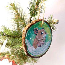 Load image into Gallery viewer, a christmas wood ornament, hand painted with the portrait of a syrian hamster, standing on the snow, watching snowflakes fall against a green and yellow sky
