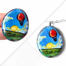 Load image into Gallery viewer, a small rock art of a red hot air balloon, floatiing in the sky over a green landscape, sun shining. available as a keepsake or pendant necklace
