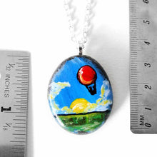 Load image into Gallery viewer, a small rock art of a red hot air balloon, floatiing in the sky over a green landscape, sun shining. available as a keepsake or pendant necklace
