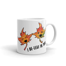 Load image into Gallery viewer, A 11 oz white ceramic mug, printed with art of two maple leaves with happy faces, and the words. "I be-leaf in you"
