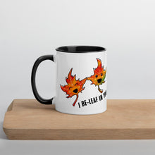 Load image into Gallery viewer, Ah 11 oz white ceramic mug with black handle and interior, printed on the front and back with an illustration of two smiling maple leaves, and the words, "I be-leaf in you"
