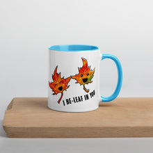 Load image into Gallery viewer, Ah 11 oz white ceramic mug with blue handle and interior, printed on the front and back with a graphic of two smiling maple leaves, and the words, "I be-leaf in you"
