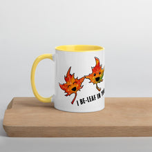 Load image into Gallery viewer, Ah 11 oz white ceramic mug with yellow handle and interior, printed on the front and back with a graphic of two smiling maple leaves, and the words, "I be-leaf in you"
