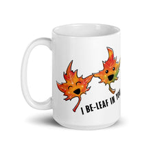 Load image into Gallery viewer, A 15 oz white ceramic mug, printed with art of two maple leaves with happy faces, and the words. "I be-leaf in you"
