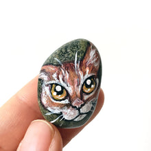 Load image into Gallery viewer, a small beach rock painted with of an orange tabby cat with golden yellow eyes, available as either a keepsake or a pendant necklace
