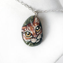 Load image into Gallery viewer, a small beach rock painted with of an orange tabby cat with golden yellow eyes, available as either a keepsake or a pendant necklace
