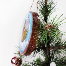 Load image into Gallery viewer, A holiday ornament with art of a chicken, sitting on snow as snowflakes fall. The ornament is painted in blues and reds.
