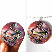 Load image into Gallery viewer, a wood circle pendant, hand painted, depicting the zodiac sign sagittarius: two hands hold a bow, with an arrow, ready to fire

