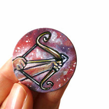 Load image into Gallery viewer, a wood circle pendant, hand painted, depicting the zodiac sign sagittarius: two hands hold a bow, with an arrow, ready to fire
