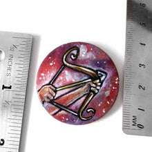 Load image into Gallery viewer, a wood circle pendant, hand painted, depicting the zodiac sign sagittarius: two hands hold a bow, with an arrow, ready to fire
