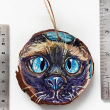 Load image into Gallery viewer, A Christmas ornament with a painting fo a blue eyed Siamese cat's face, next to two rulers to show its size: 2 15/16 x 3 1/8 inches or 7.8 x 8.4 cm
