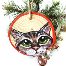 Load image into Gallery viewer, A Christmas wood ornament, features a painting of the face of a tabby cat with green eyes, and a red border.
