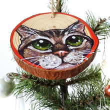 Load image into Gallery viewer, A Christmas wood ornament, features a painting of the face of a tabby cat with green eyes, and a red border.
