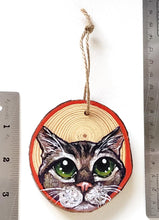 Load image into Gallery viewer, A Christmas wood ornament, features art of the face of a tabby cat with green eyes, and a red border.
