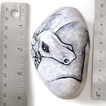 Load image into Gallery viewer, a stone hand painted with the portrait of a unicorn with purple eyes
