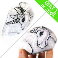 Load image into Gallery viewer, a stone hand painted with the portrait of a unicorn with purple eyes

