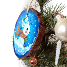 Load image into Gallery viewer, A wood Christmas ornament, hand painted with a white bunny rabbit sitting on the snow with a blue background, with an orange scarf, green mittens, and christmas lights on its ears
