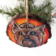 Load image into Gallery viewer, a round wood ornament, hand painted with a portrait of a Yorkshire Terrier's smiling face, against a background of red and oranges.
