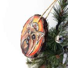 Load image into Gallery viewer, a round wood ornament, hand painted with a portrait of a Yorkshire Terrier's smiling face, against a background of red and oranges.
