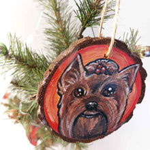 Load image into Gallery viewer, a round wood ornament, hand painted with a portrait of a Yorkshire Terrier's smiling face, against a background of red and oranges.
