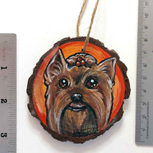 Load image into Gallery viewer, a round wood ornament, hand painted with a portrait of a Yorkshire Terrier's smiling face, against a background of red and oranges.
